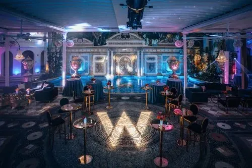 Dark event lounge with a lit logo on a stage and standing tables