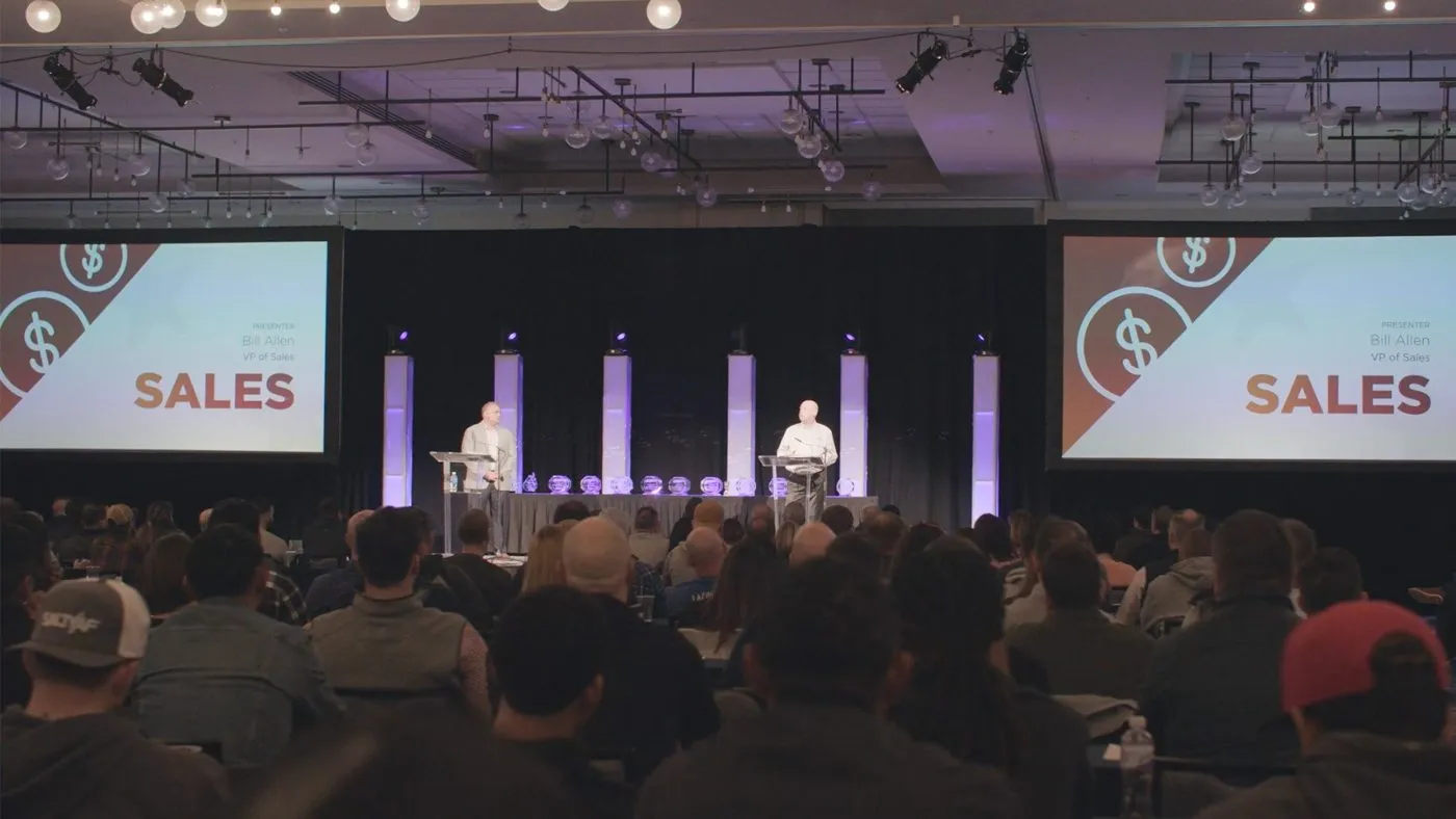 Sales meeting stage with large screens and a seated audience