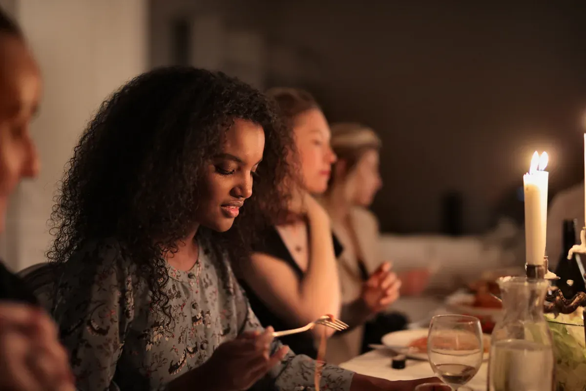 Colleagues sit shoulder to shoulder along a long, candlelit dinner table, quietly tucking into plated food as the evening settles in. A seated dinner gives everyone the same table and an unhurried evening together.