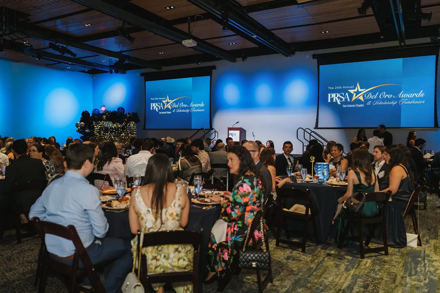 Ballroom with seated guests facing stage screens at a large dinner