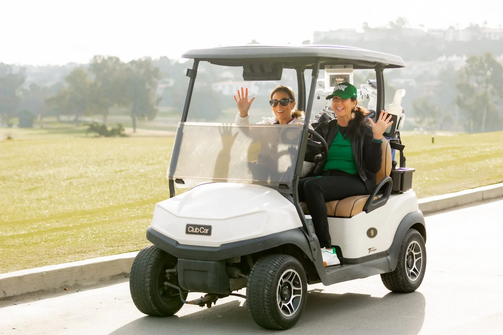Two guests waving from a golf cart on a golf course during a company event