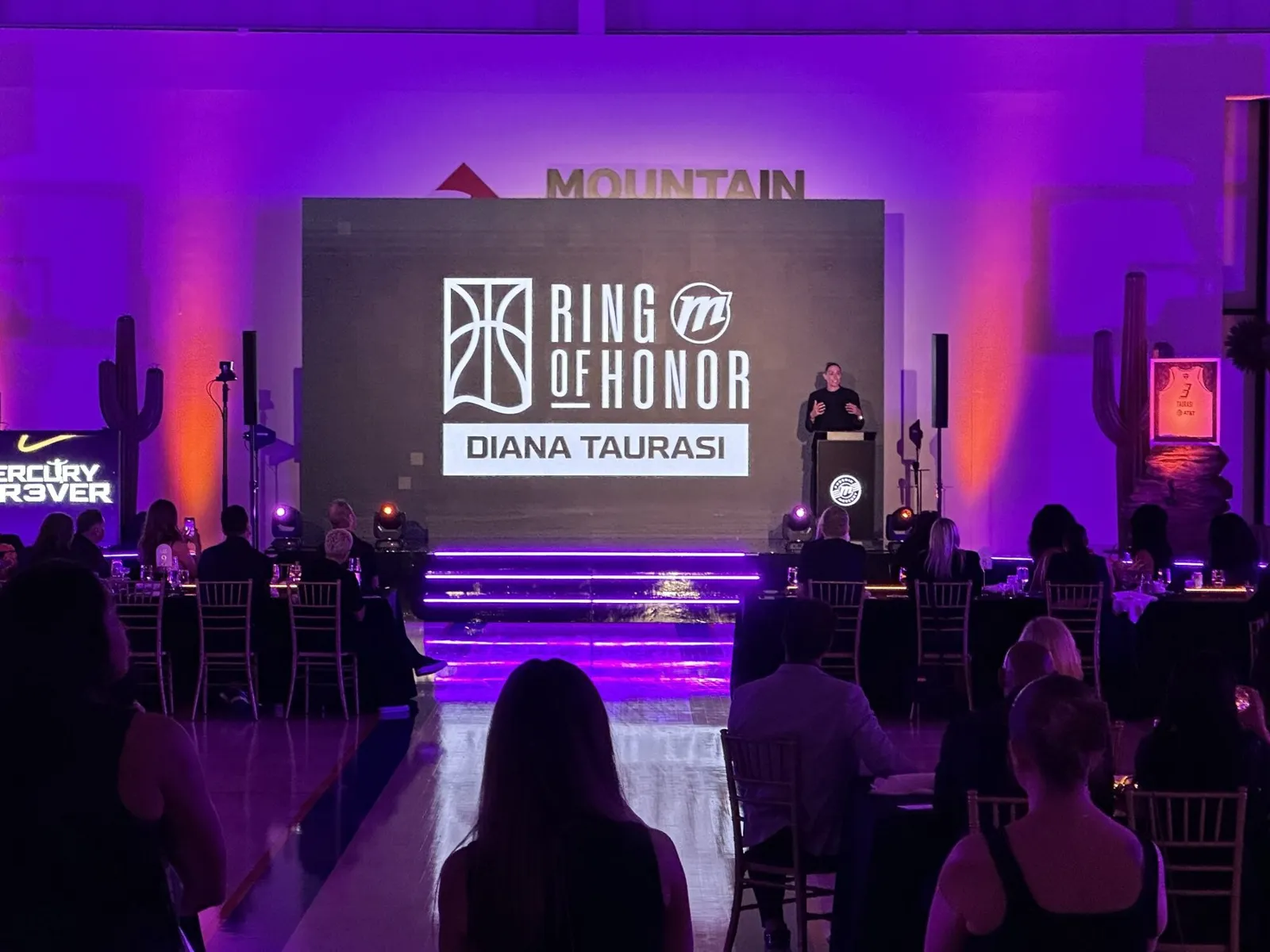 Diana Taurasi speaking in front of the Ring of Honor LED wall at her retirement dinner in Phoenix