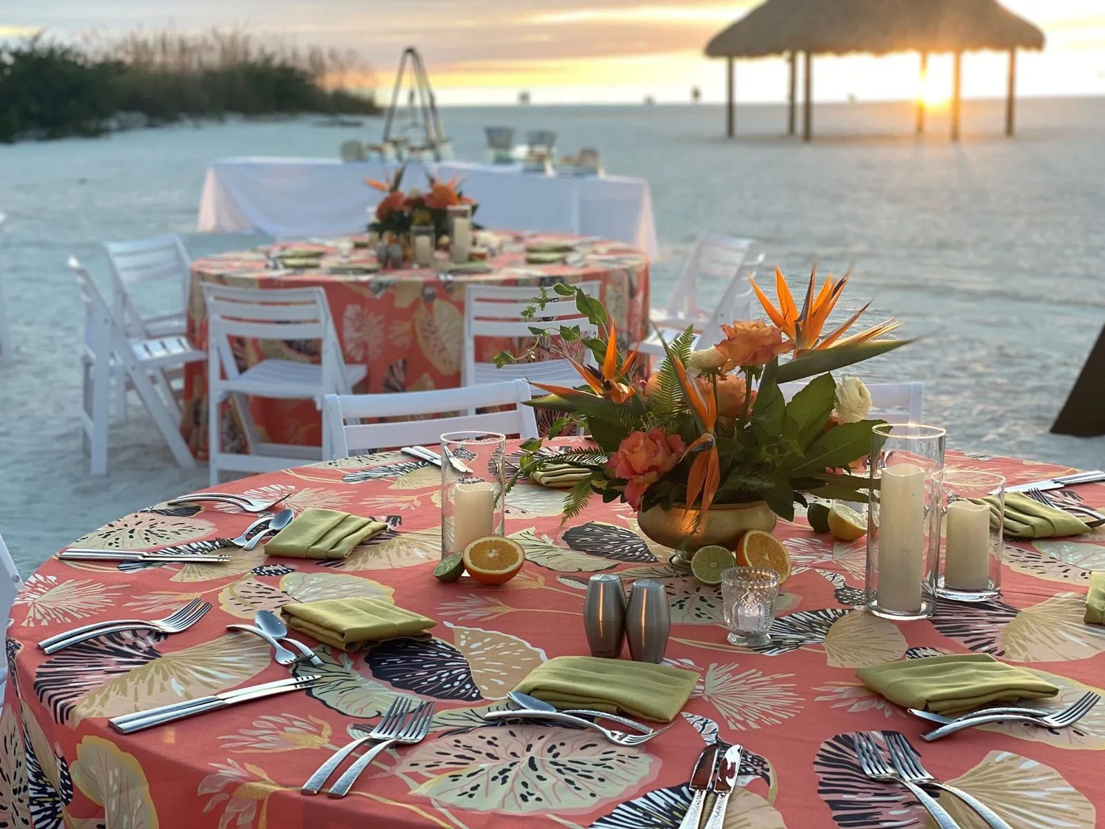 Beachfront dinner tables with tropical centerpieces at sunset