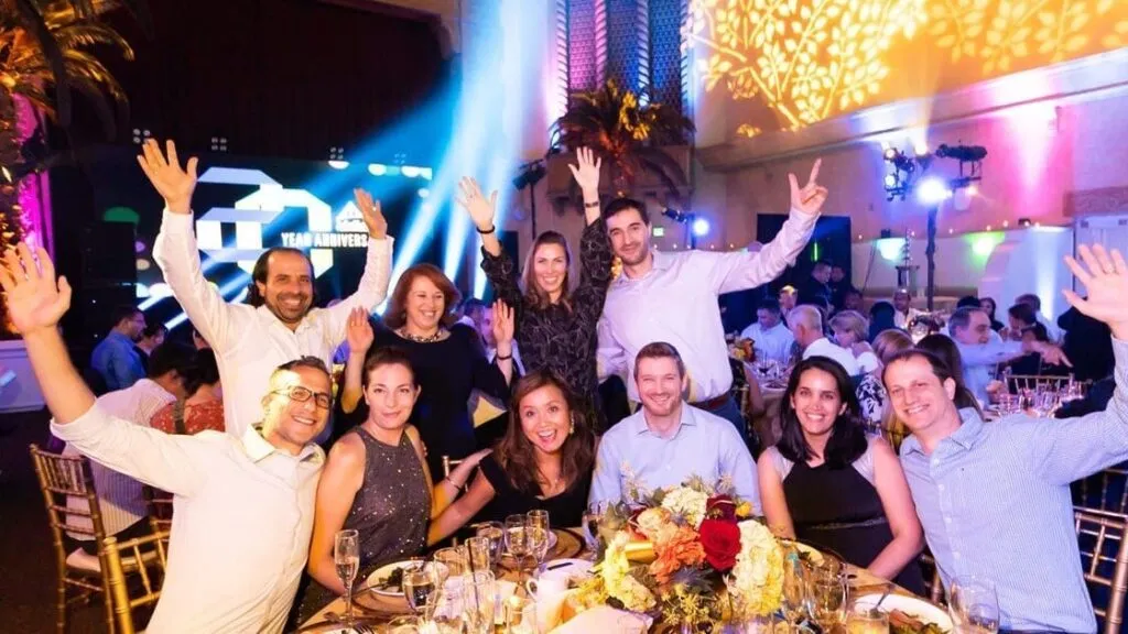 Employees cheering at a dinner table under a stage glow at a company event