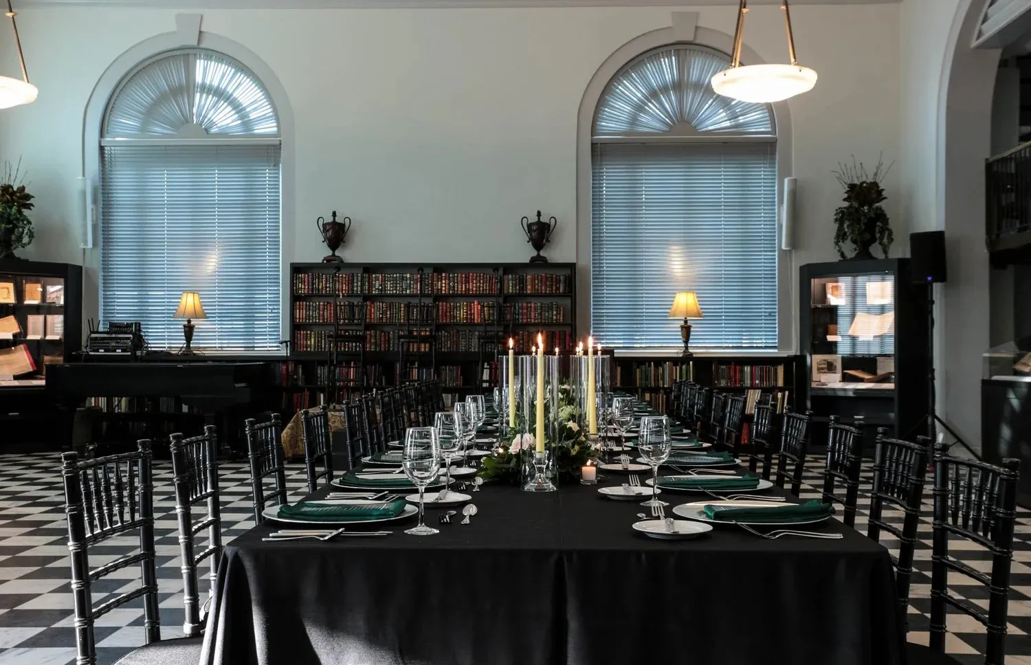 Long dinner table set in a library with arched windows and candlelight