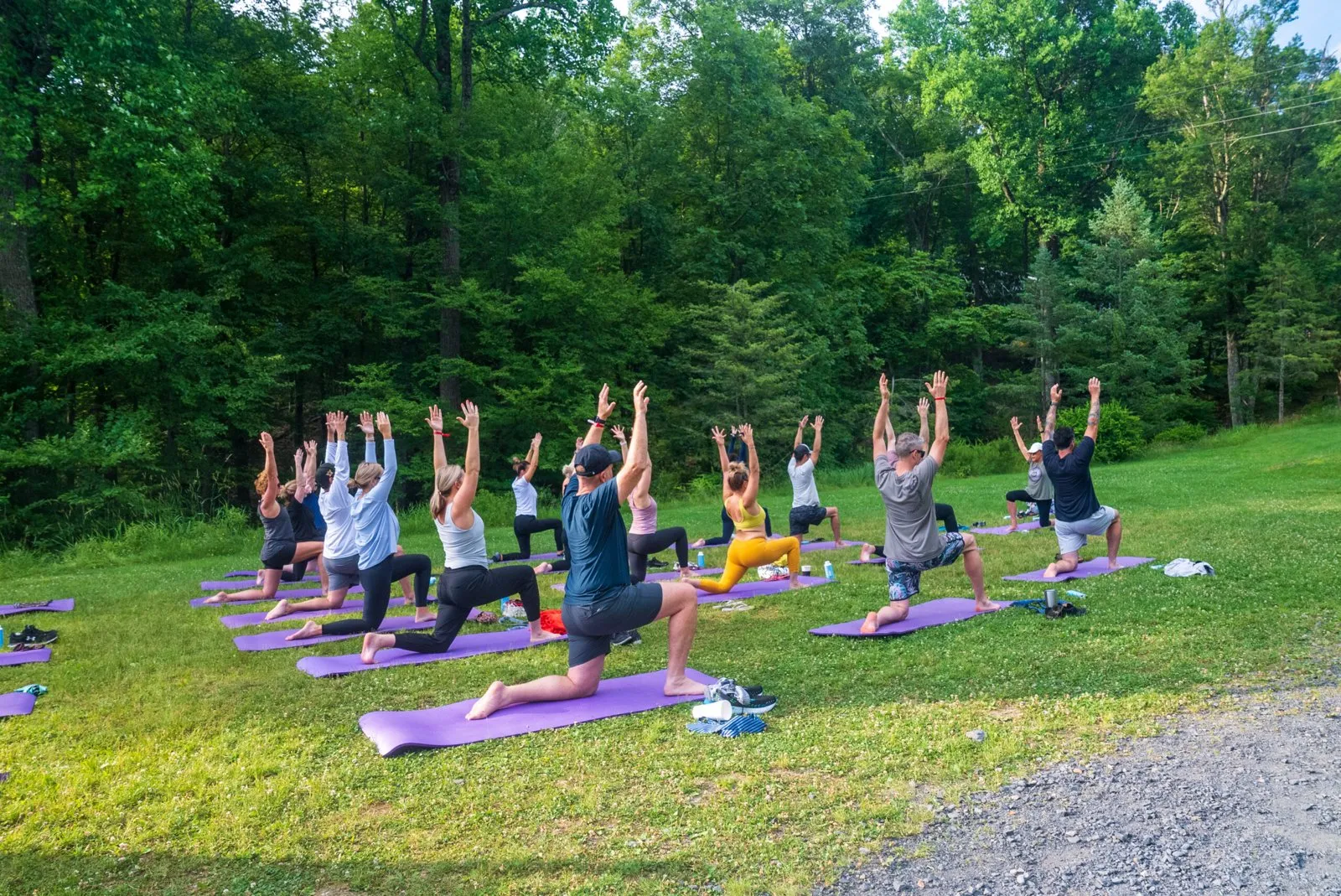 Attendees in a group yoga session on a tree-lined lawn