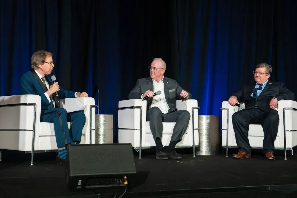 Three panelists seated on a stage during a corporate panel discussion