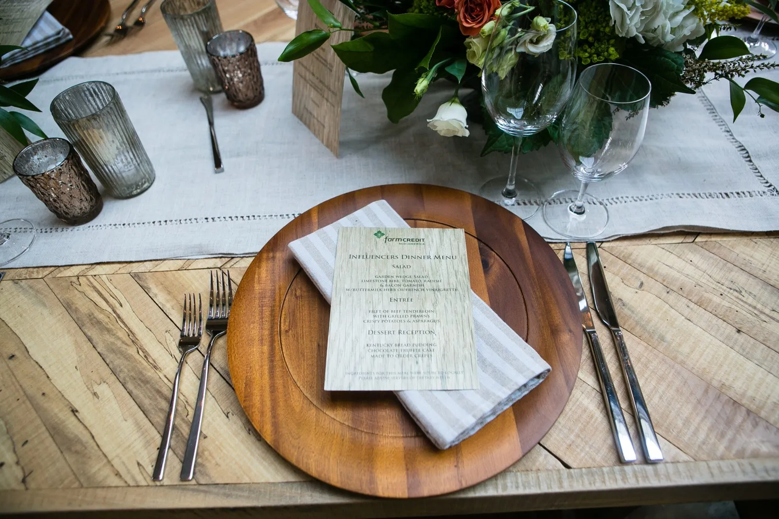Rustic dinner place setting with a wooden charger, printed menu and candles