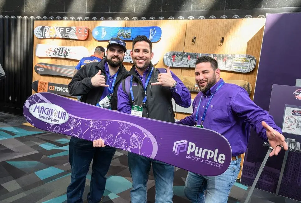 Three men holding a purple branded board at a trade show booth