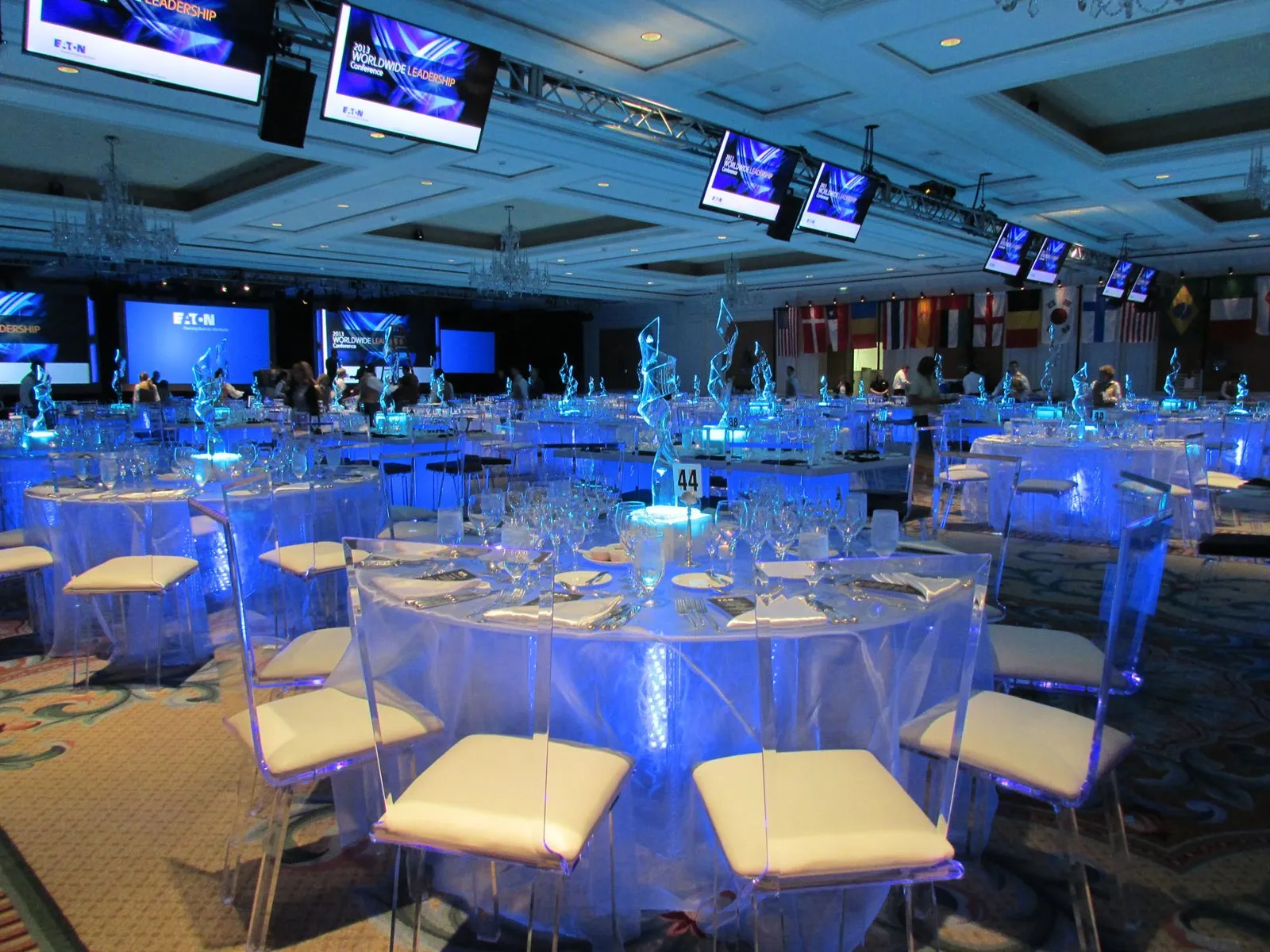Ballroom dinner with blue uplighting, white lounge seating and screens