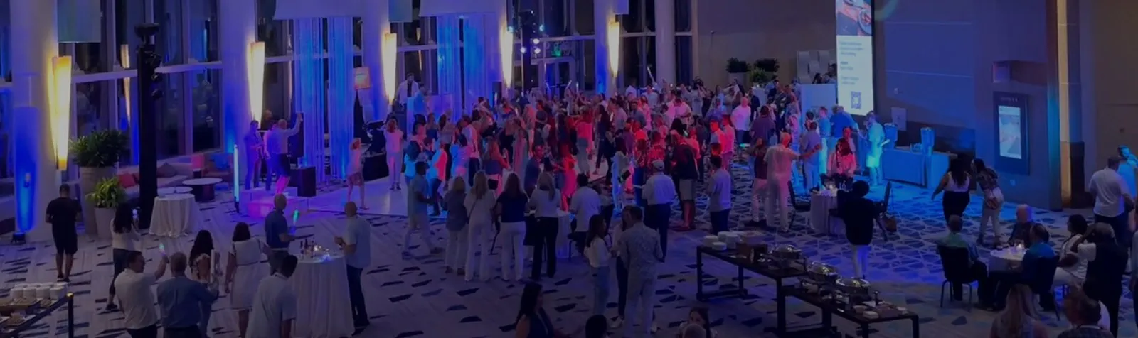 Large group of guests at an evening reception in a hotel atrium with blue lighting