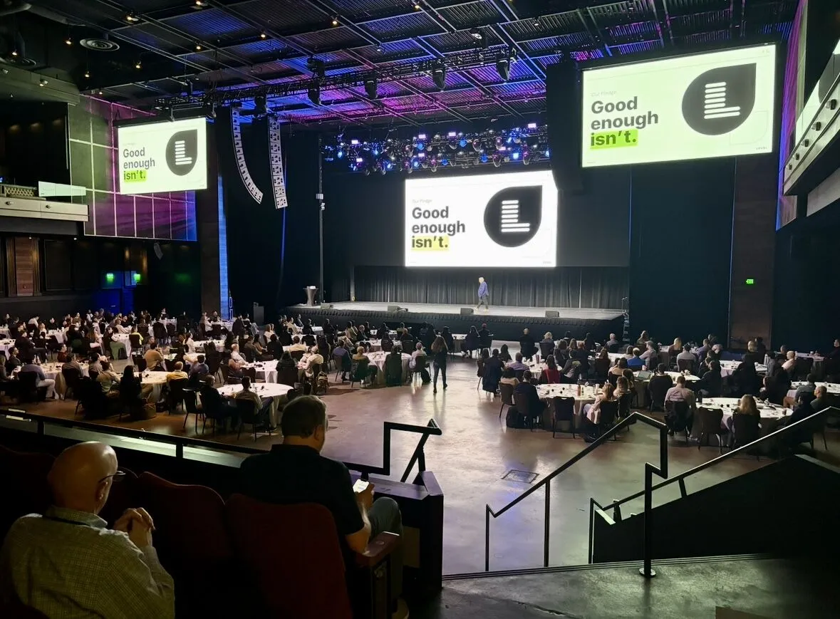 Theater set with round tables facing branded stage screens for a two-day summit at Chelsea Theater, Las Vegas
