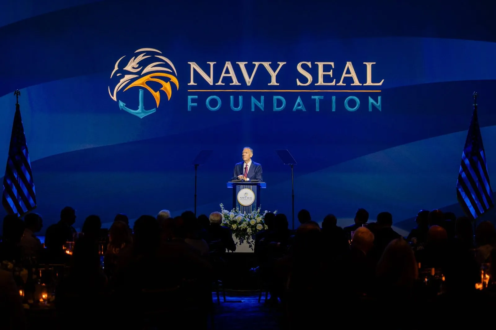 Speaker at a podium on a lit stage during a gala program