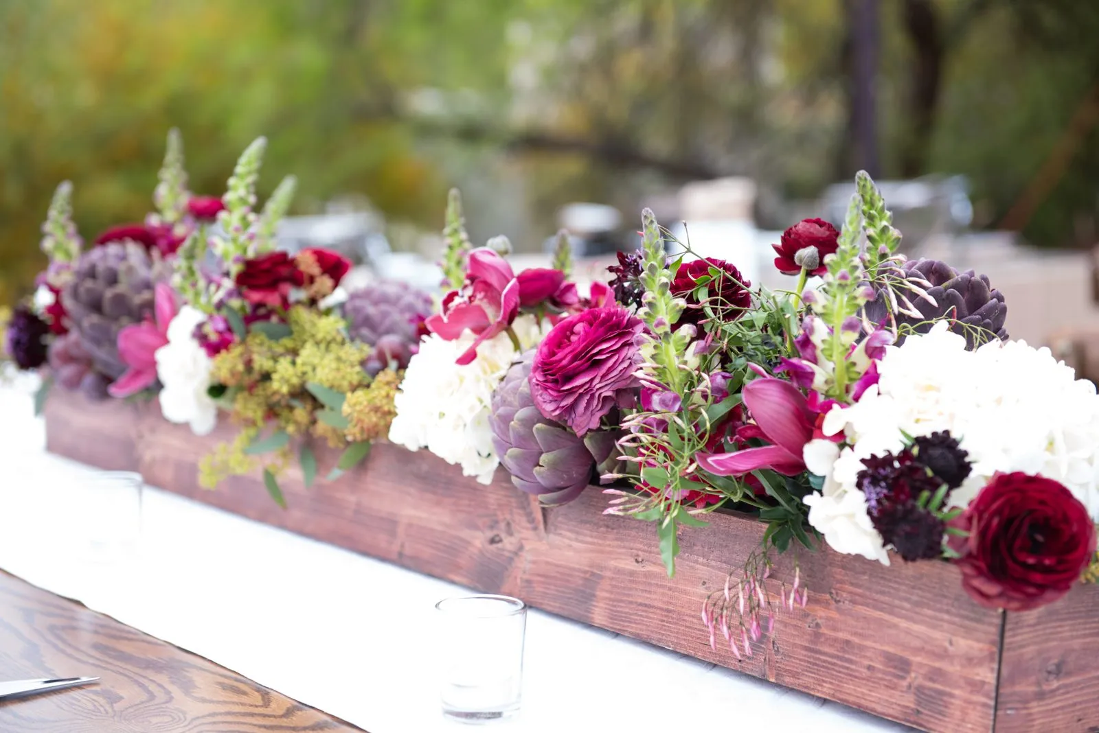 Long wooden table with a low floral centerpiece set up outdoors