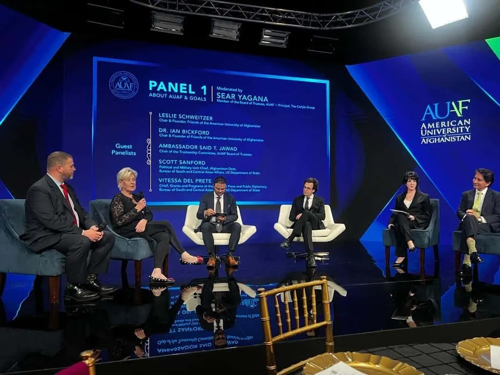 Panel of speakers seated on a blue lit stage with a large LED wall