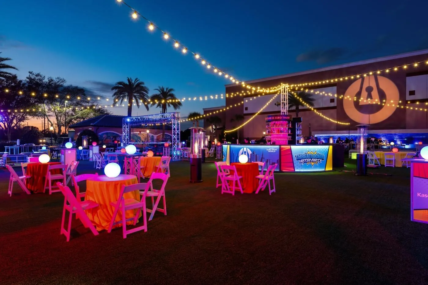 Evening reception on grass with tables, string lights, palm trees and colorful lighting