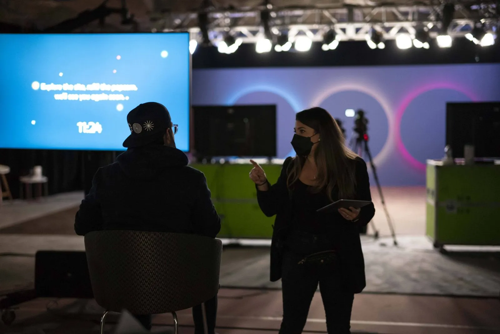 Production crew member holding a tablet beside screens at a brand event