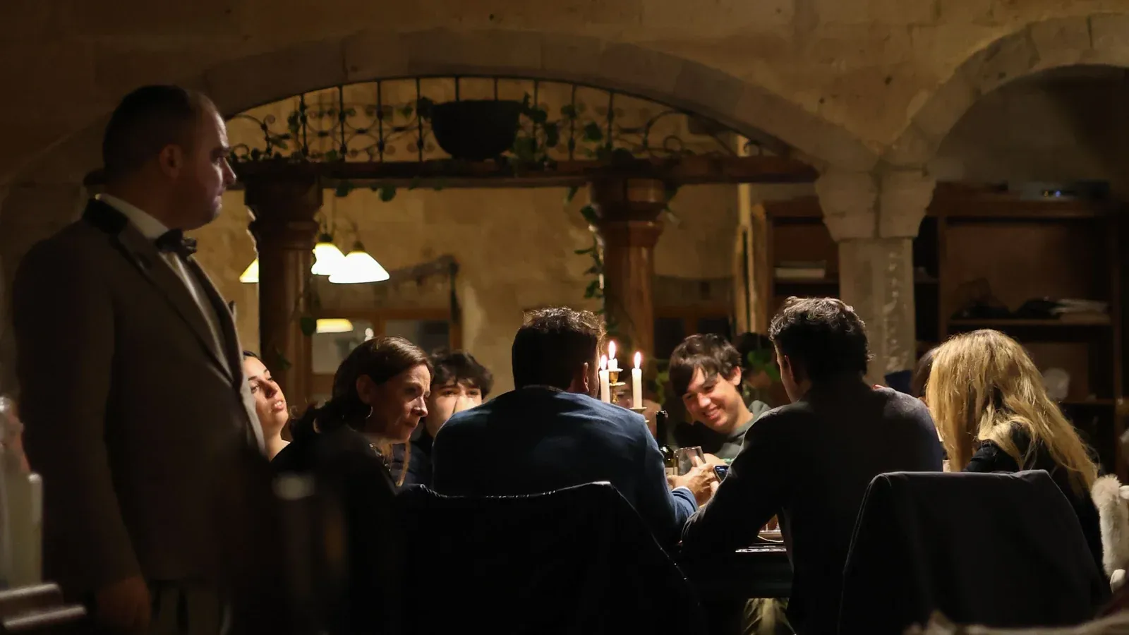 A group gathers around a candlelit table under stone arches and pendant lamps for a group dinner during an incentive trip.