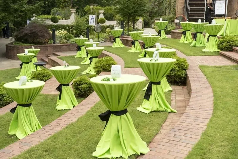 Cocktail tables with green linens set on a garden lawn for a reception