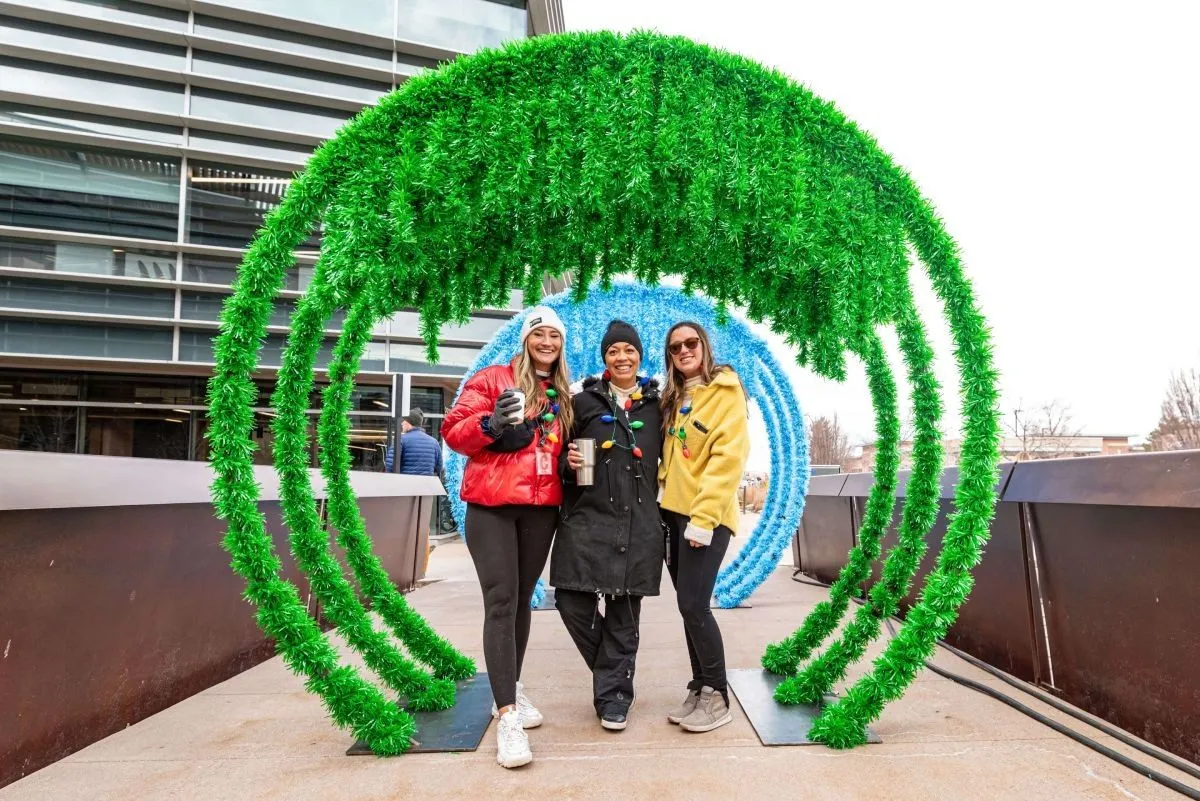Three team members posing under a green photo arch installation