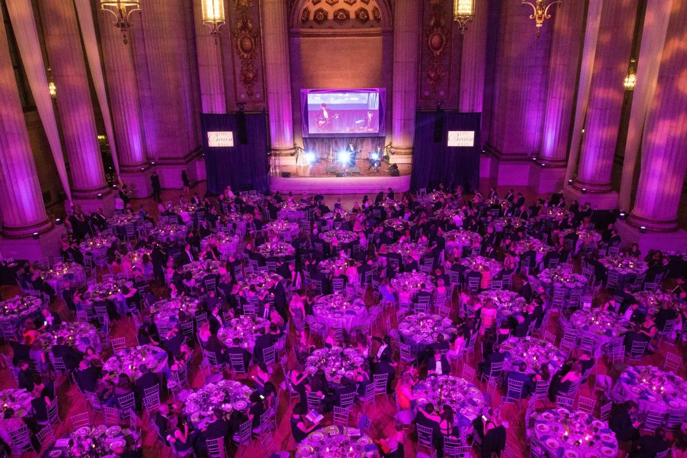 Ballroom filled with round tables and purple uplighting