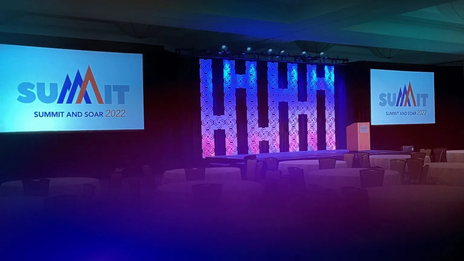 Summit stage with a lit backdrop and side screens in a meeting room