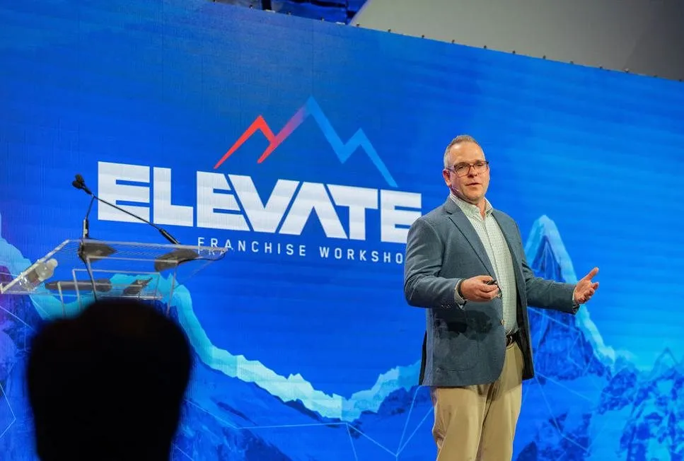 Speaker on stage in front of an Elevate Franchising Workshop screen