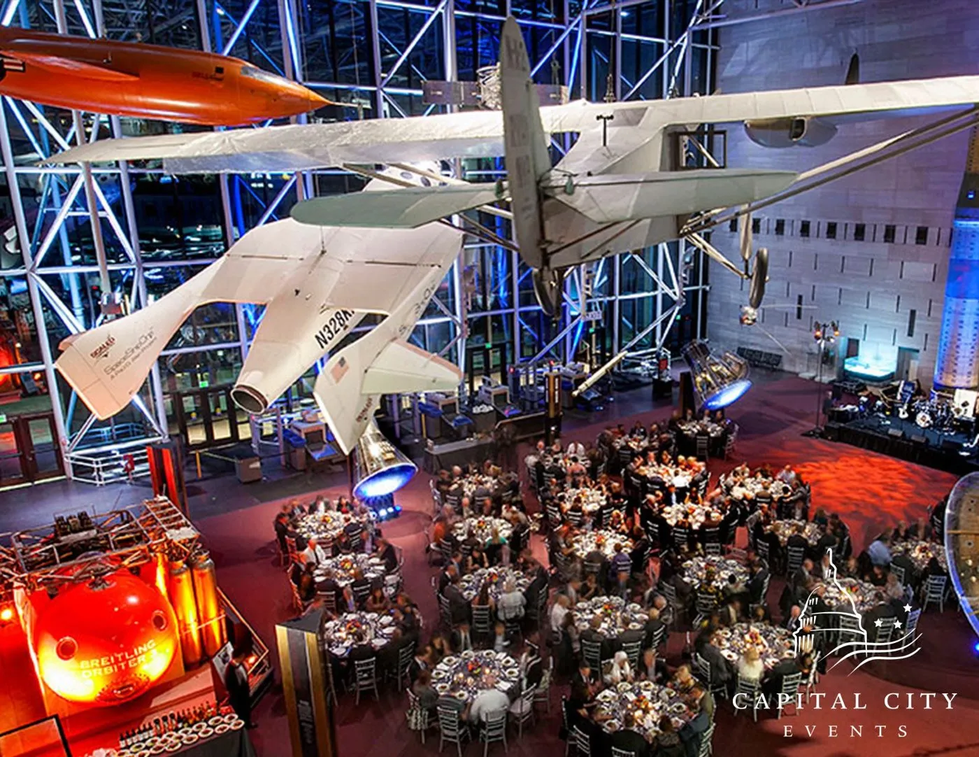 Dinner tables set beneath suspended aircraft in an aviation museum hall