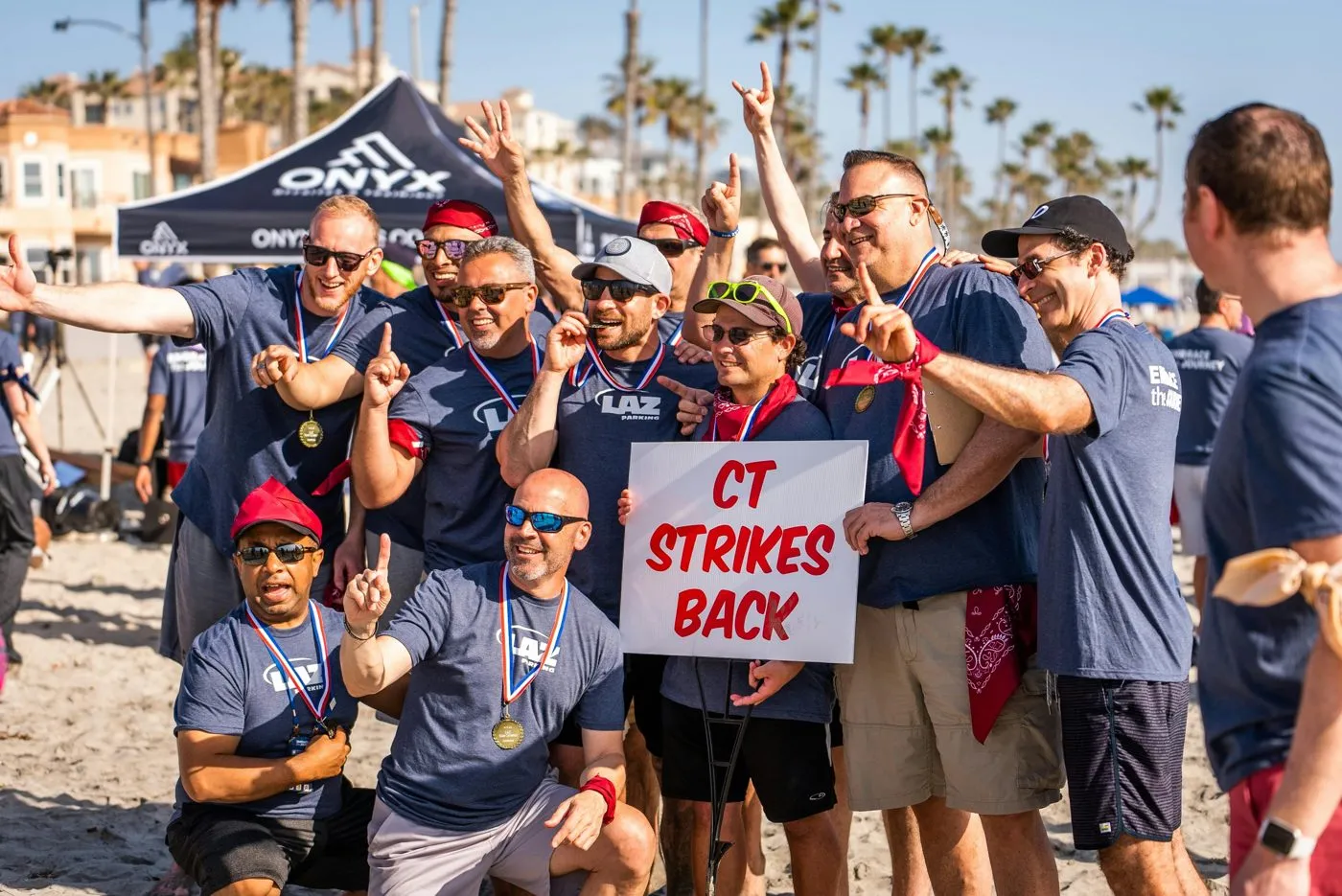Team in matching shirts cheering on a beach holding a team sign