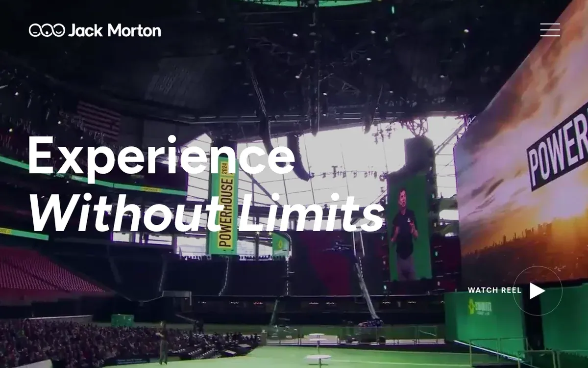 Jack Morton homepage hero with the headline Experience Without Limits over a stadium event, a tall screen reading Powerhouse, a presenter shown on a green video wall, and a Watch Reel button