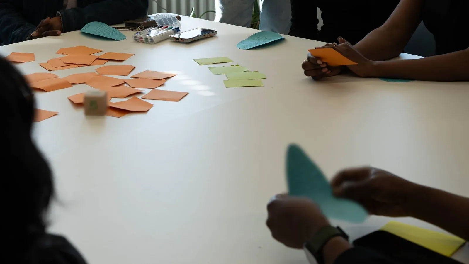 Hands move colorful idea cards and sticky notes across a white table during a hands-on workshop at a company offsite.