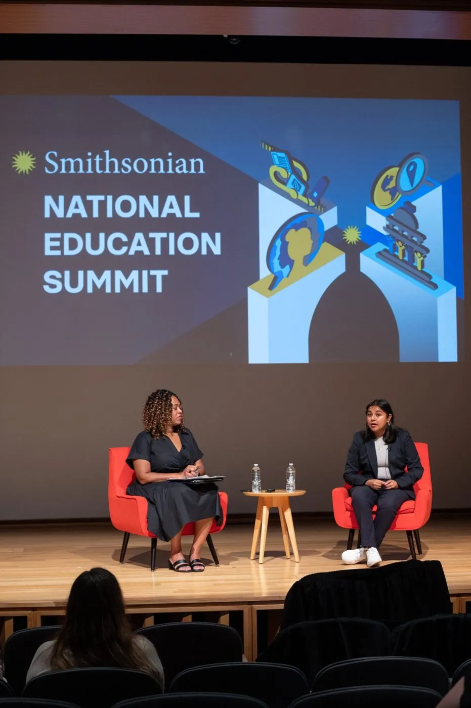 Two speakers in conversation on an education summit stage
