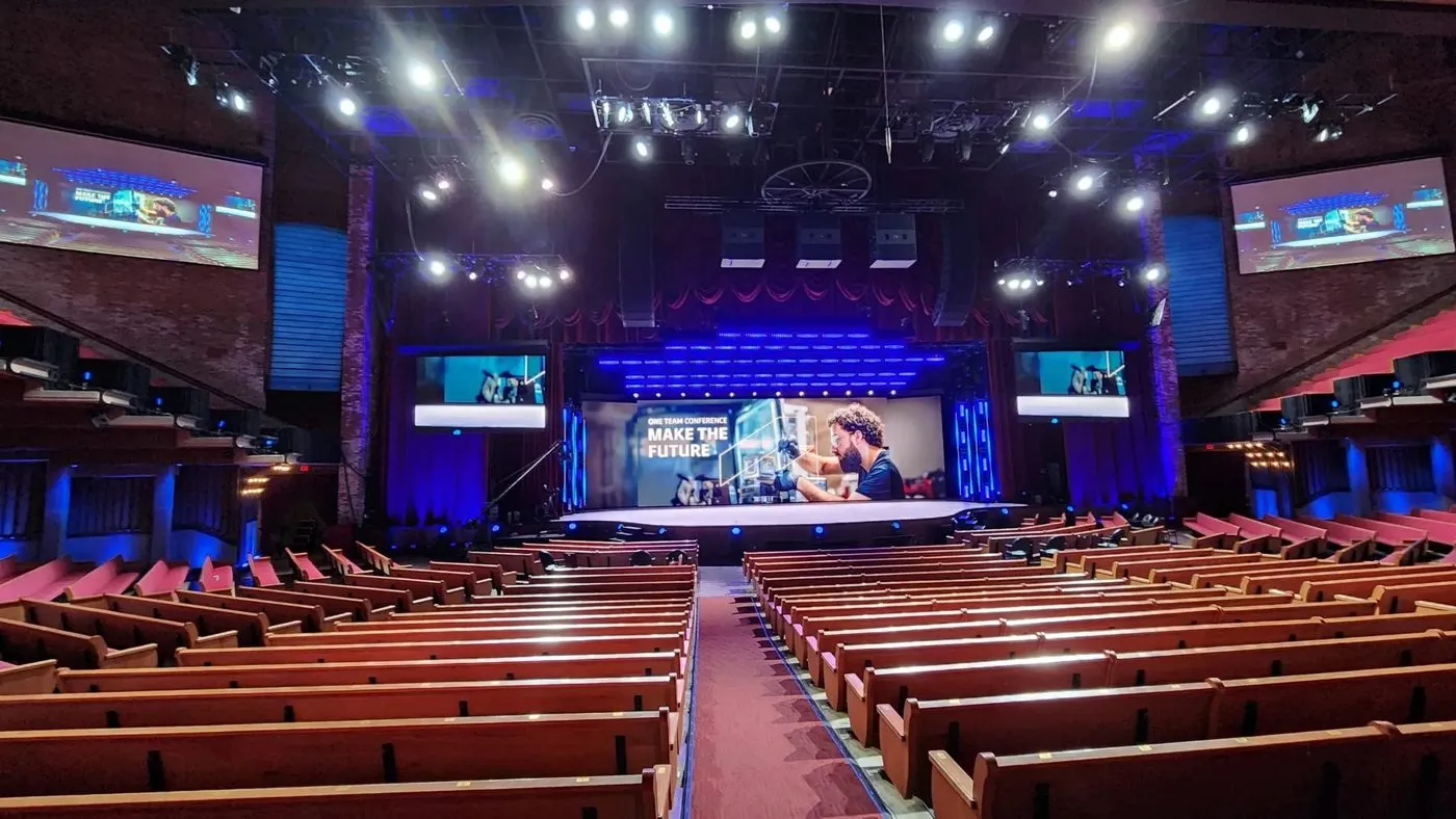 Conference hall with stage screens and lighting over seated attendees