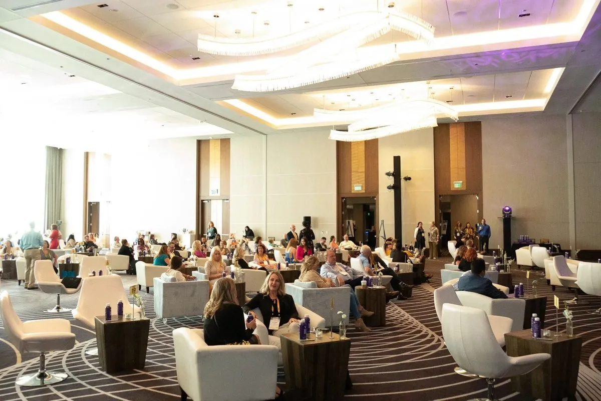 Large meeting room with attendees seated in white armchairs and lounge seating