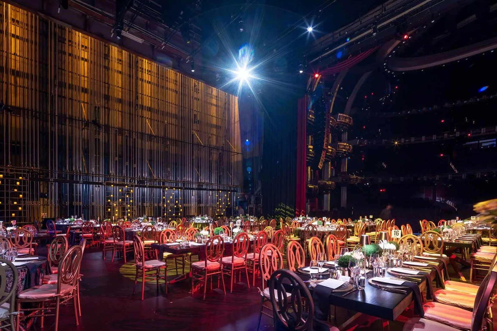 Round tables set for dinner in a dark venue with stage lighting