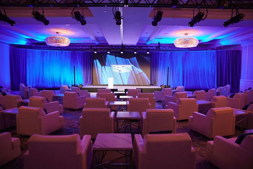 Lounge seating facing a blue-lit stage and screen in a hotel meeting room