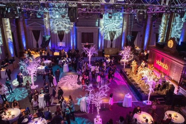 Reception tables and lit trees under purple lighting at a corporate evening event