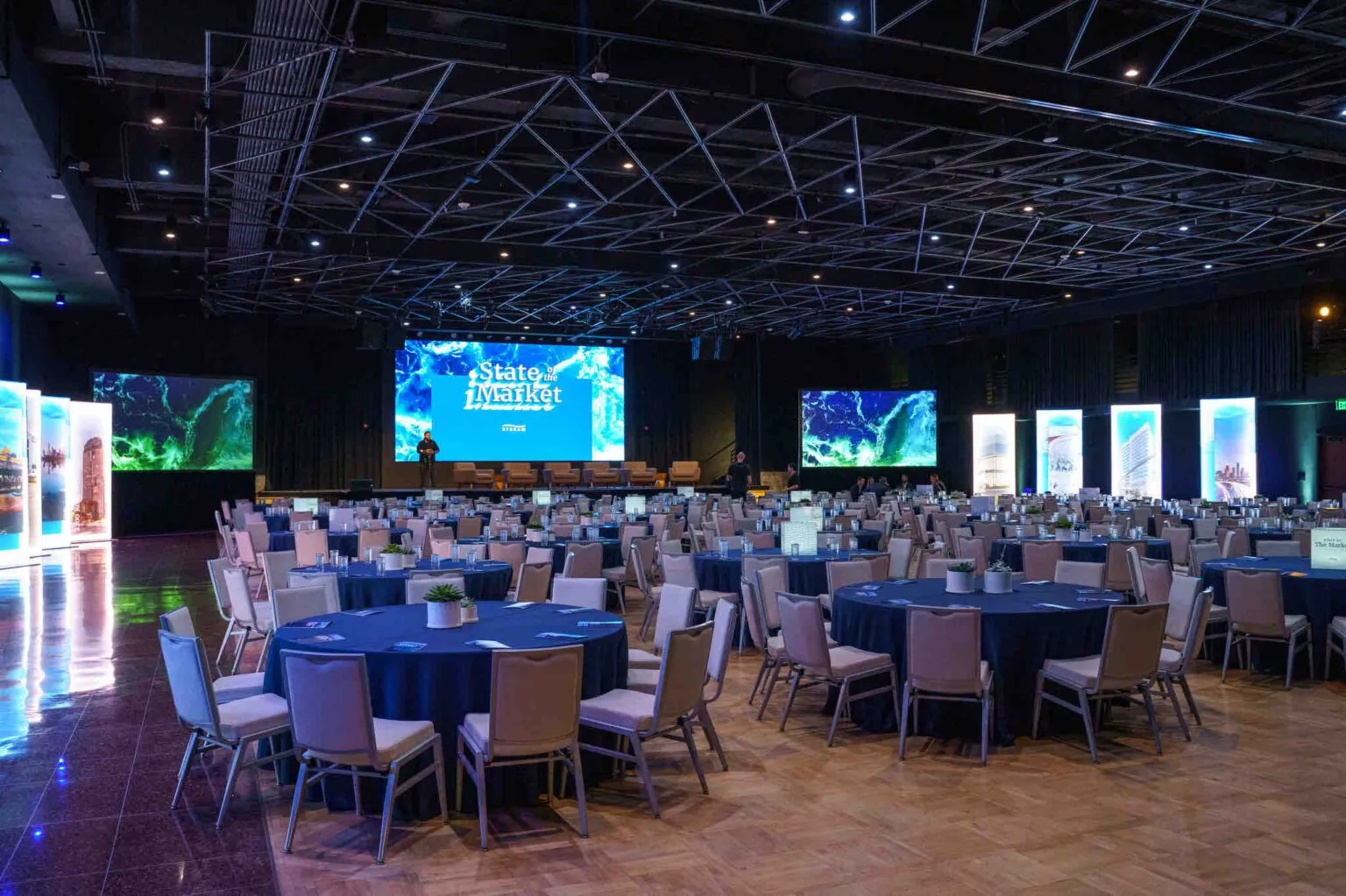 Large ballroom with round tables and screens set for an annual market meeting