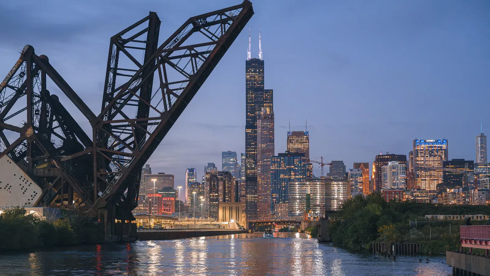 The Chicago skyline at dusk beyond a raised steel bridge over the Chicago River
