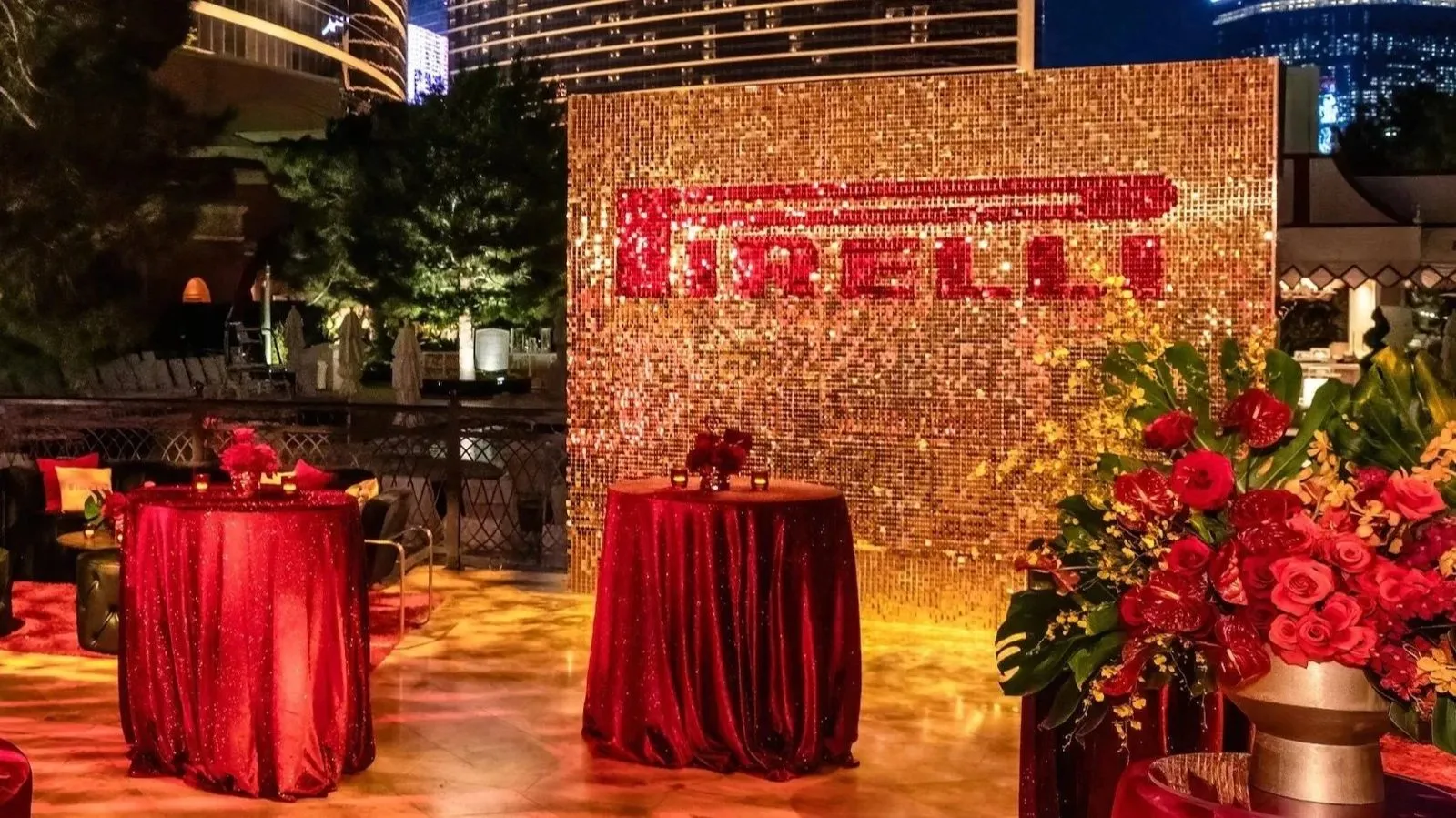 Red cocktail tables in front of a gold sparkle wall at a corporate holiday reception