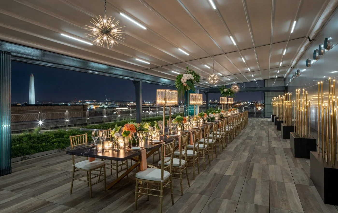 Long banquet tables set on a rooftop event space overlooking the city at night