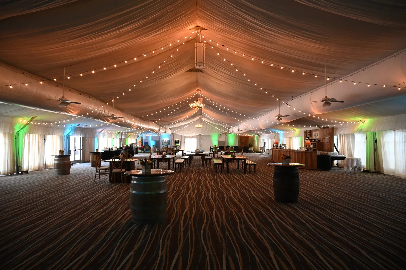 Large tented hall with a draped ceiling and wood floor set for a reception