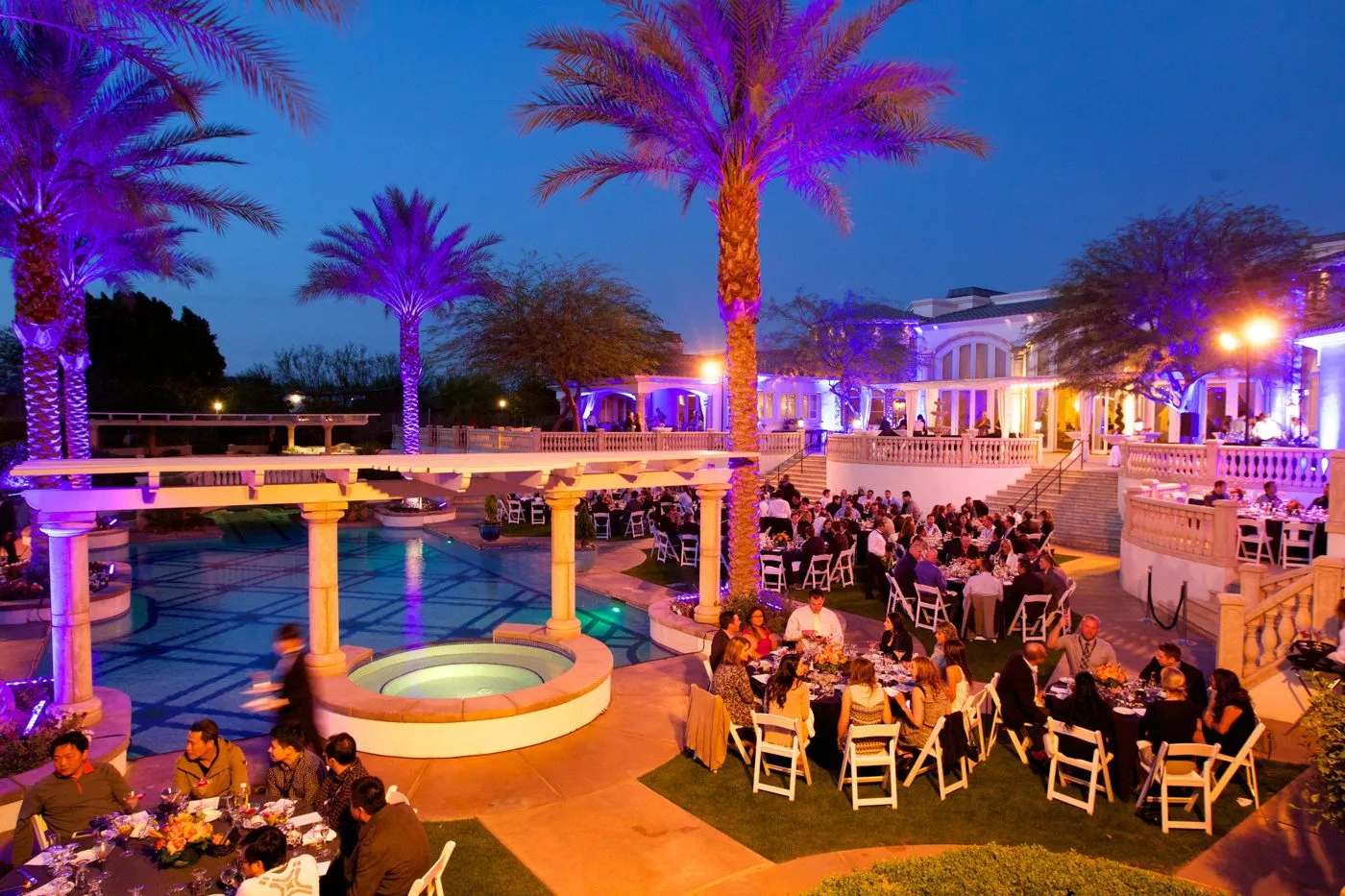 Evening group dinner on a terrace with a pool and palm trees lit in purple