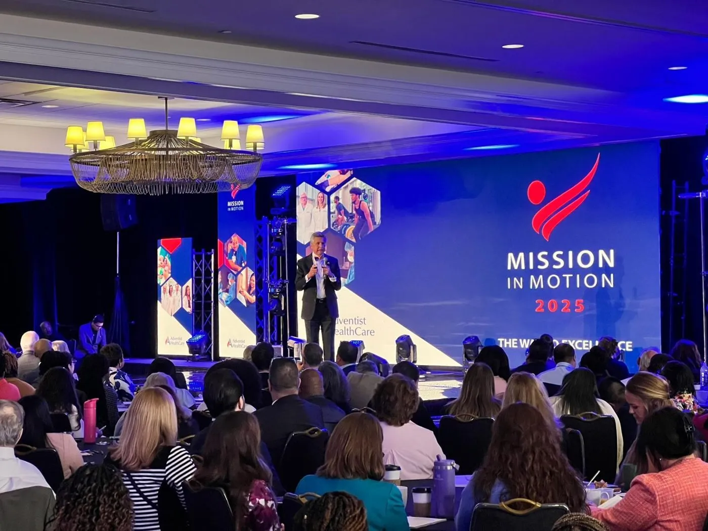 General session audience facing a stage with a large branded screen