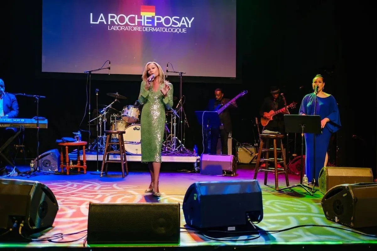 Live performance on a lit stage in front of a branded video screen with a band