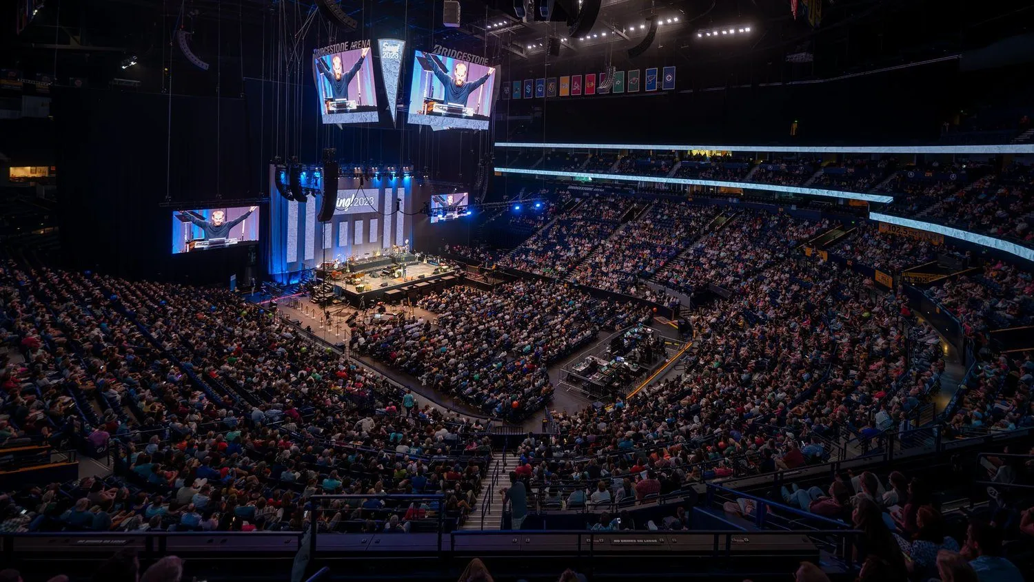 Thousands of attendees seated in an arena facing a stage for a corporate conference