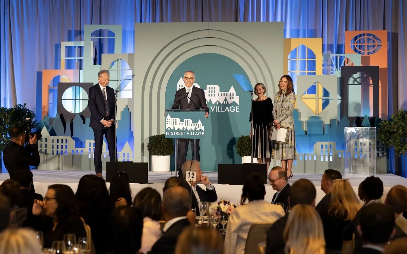 Speakers at a podium on an illustrated stage in front of a seated audience
