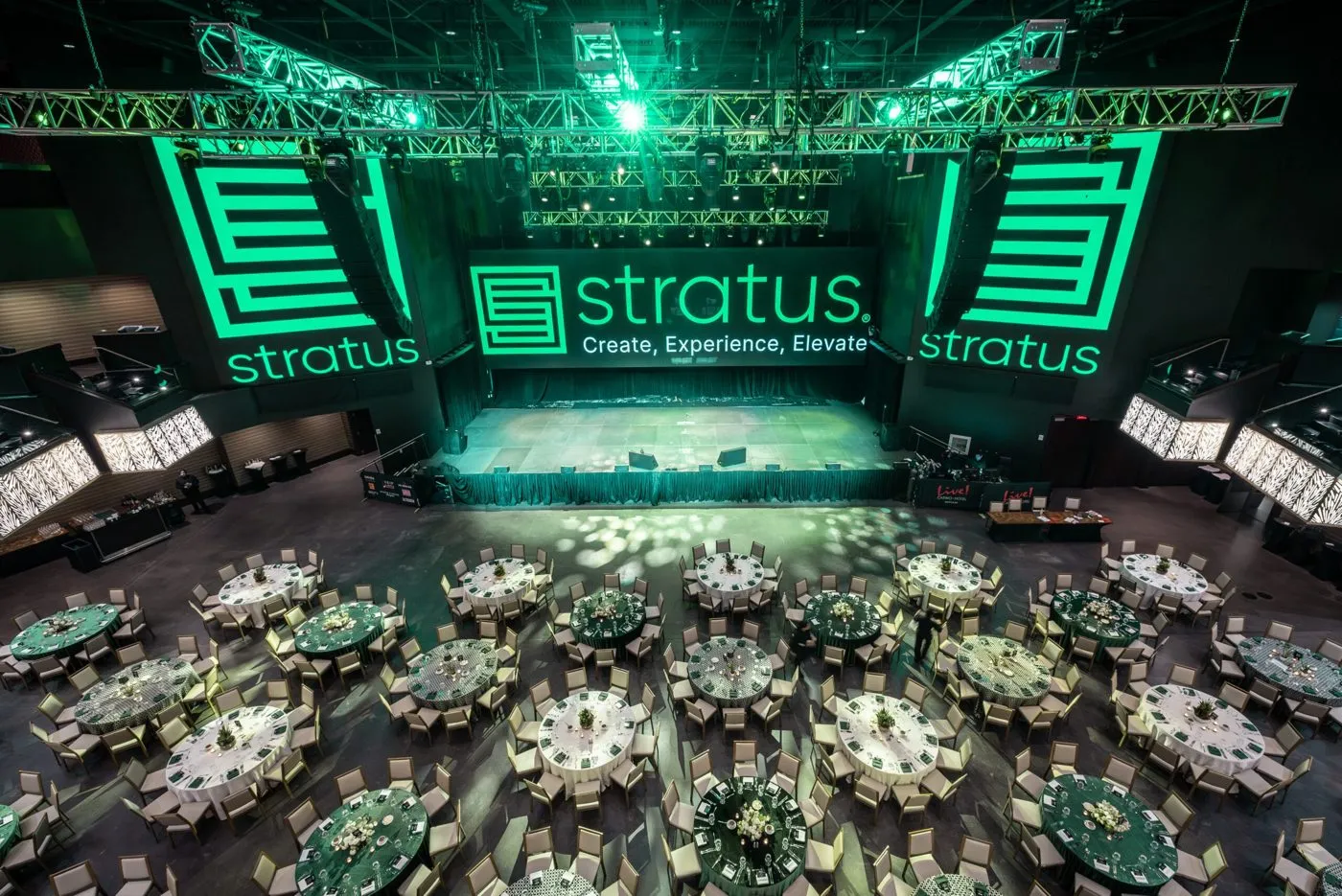 Gala ballroom with round tables and a lit stage with branded screens