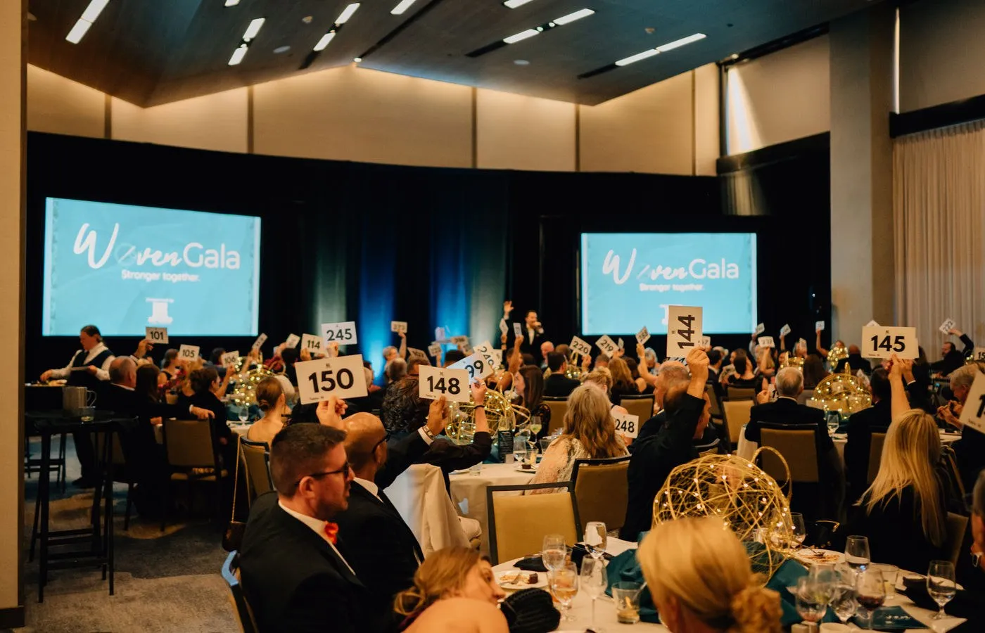 Gala guests seated at round tables in a ballroom facing large screens