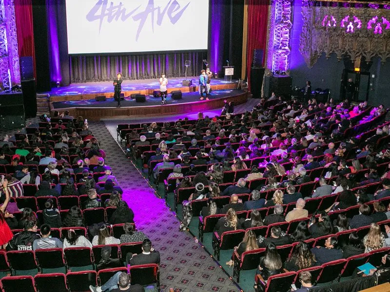 Seated audience facing a stage lit in purple light